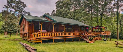 A wooden cabin with a porch, surrounded by trees.