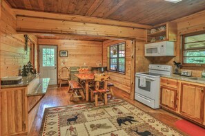 A wooden cabin kitchen with a dining table, chairs, a microwave, and a stove.