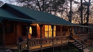 Een vakantiehuis in blokhutstijl met een veranda, houten terras en een trap naar de bovenverdieping.