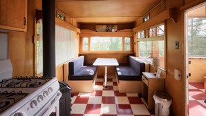 Un intérieur de camping-car compact comprenant un coin cuisine, un espace repas avec une table et des bancs, et un sol à carreaux.