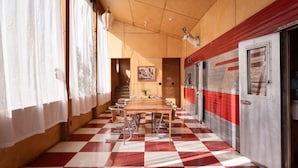 Un couloir doté d’un sol à carreaux, une longue table entourée de chaises et une porte ornée d’une bande rouge.