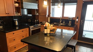 Una cocina moderna con armarios de madera, encimera negra y una isla central con una botella de vino y copas.