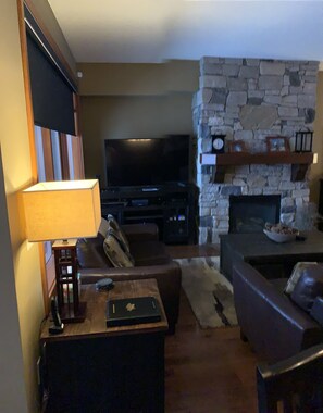 Ein Wohnzimmer mit Kamin aus Stein, einem Flachbildfernseher und einer Couch.