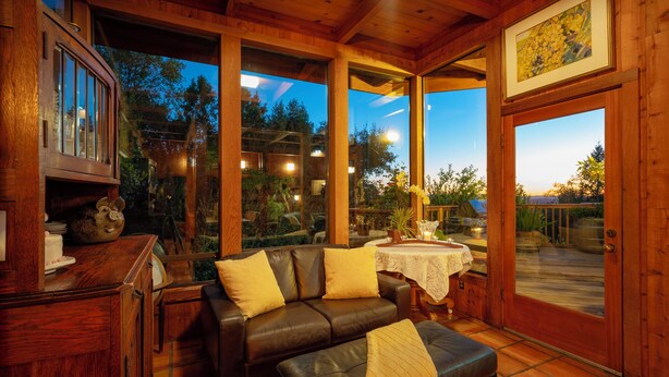 Una habitación acogedora con un sofá de cuero, una mesa con mantel blanco y ventanas amplias que ofrecen vistas al exterior.