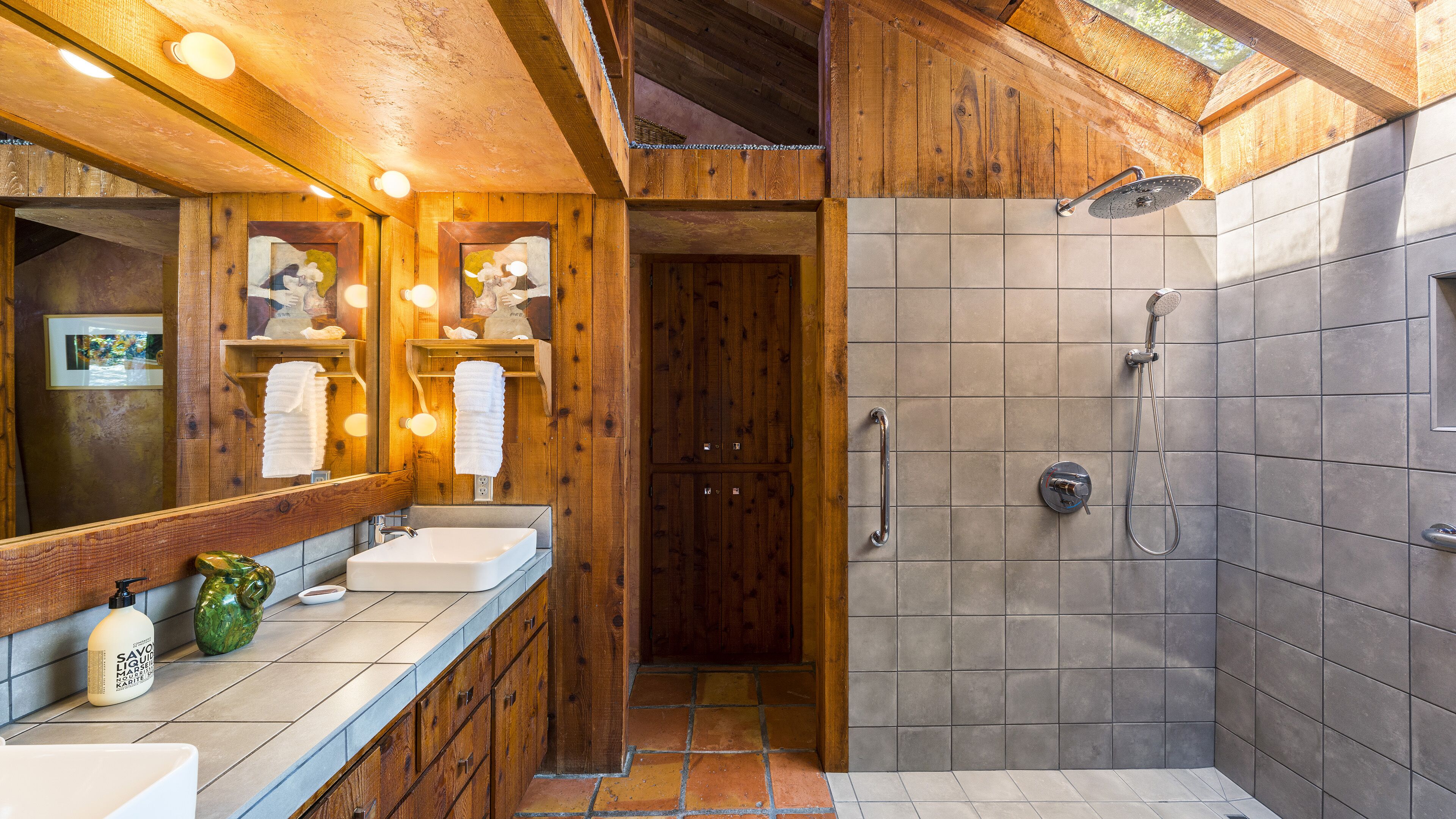 Een houten badkamer met twee wastafels, een douche en een spiegel.