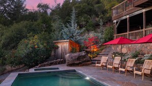 Un área de piscina con cubierta de piedra, sillas de madera y una estructura de madera con balcón.