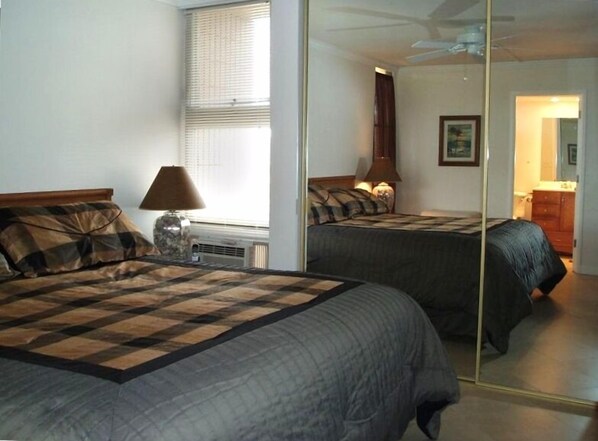 A bedroom with two beds, a mirror, a lamp, and a window with blinds.