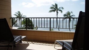Un balcon avec deux chaises, une vue sur la mer et des palmiers.