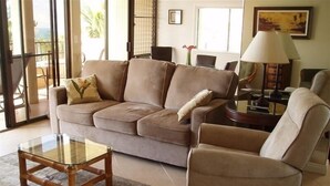 Un salon avec un canapé beige, une table basse en verre et un fauteuil assorti.