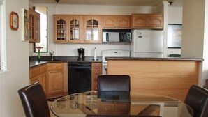 Une cuisine avec des meubles en bois, un four à micro-ondes, un réfrigérateur et une table à manger en verre, accompagnée de chaises.