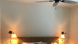 Un dormitorio con cama, dos mesitas de noche, ventilador de techo y lámparas de pared.