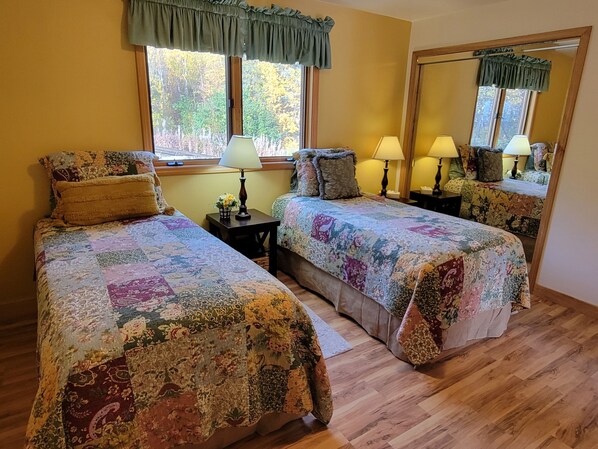 A bedroom with two beds, a large mirror, and a window with a view of trees.