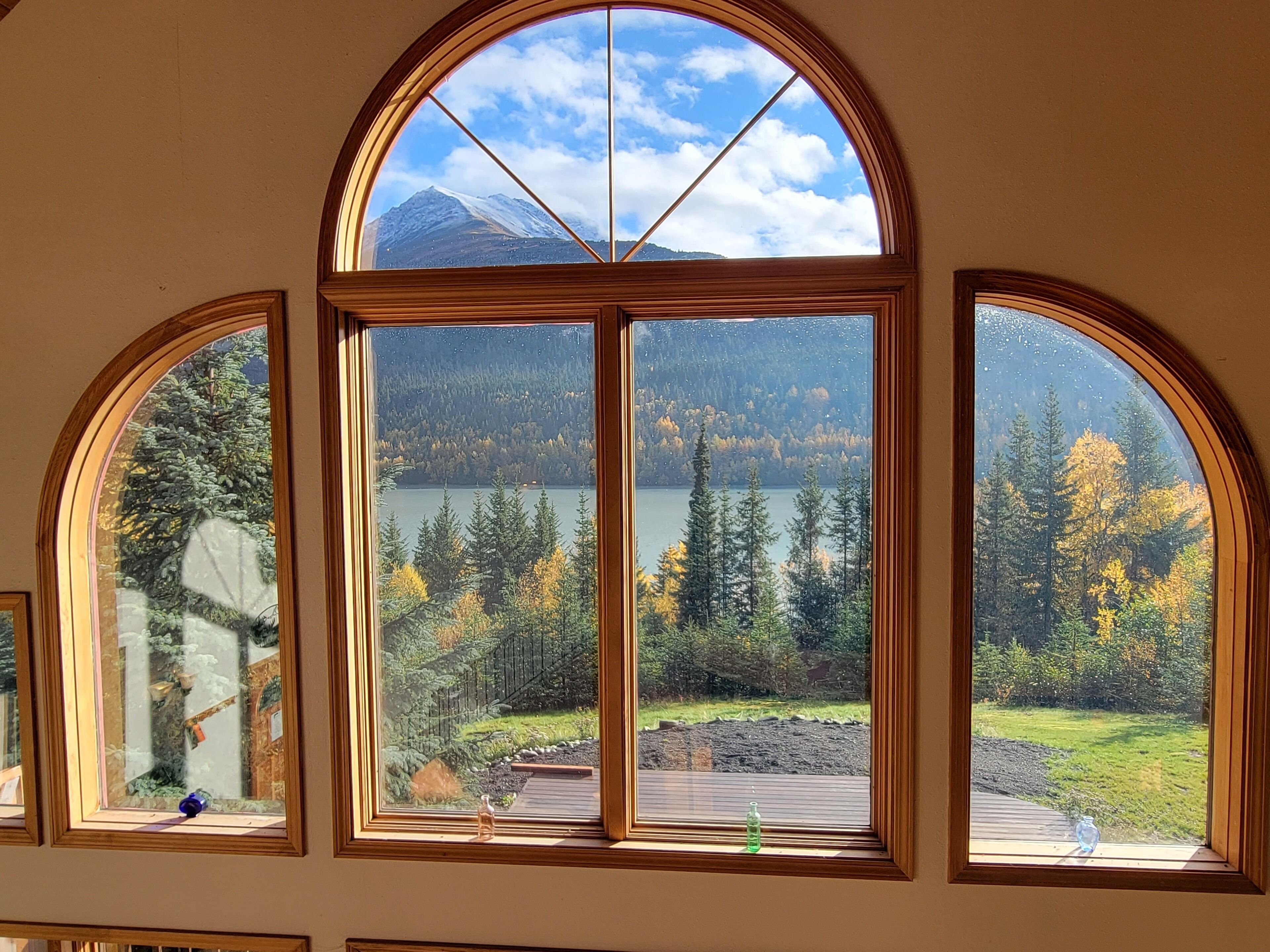 A room with a large arched window overlooking a lake and forest.