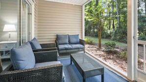 A covered patio with wicker furniture and a view of a wooded area.