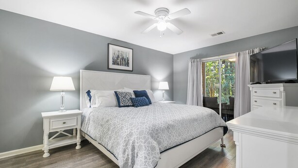 A bedroom with a bed, nightstands, a ceiling fan, a TV, and a window with curtains.