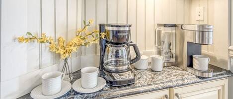 Una cocina con cafetera, hervidor y un florero con flores amarillas sobre la encimera.