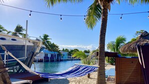 A beachside area with a hammock, a boat docked by the water, and a small wooden structure. - Deep Water Canal, Swim Spa Pool, Kayaks, Walk to Ocean Front Bars & Restaurants! (Marathon)