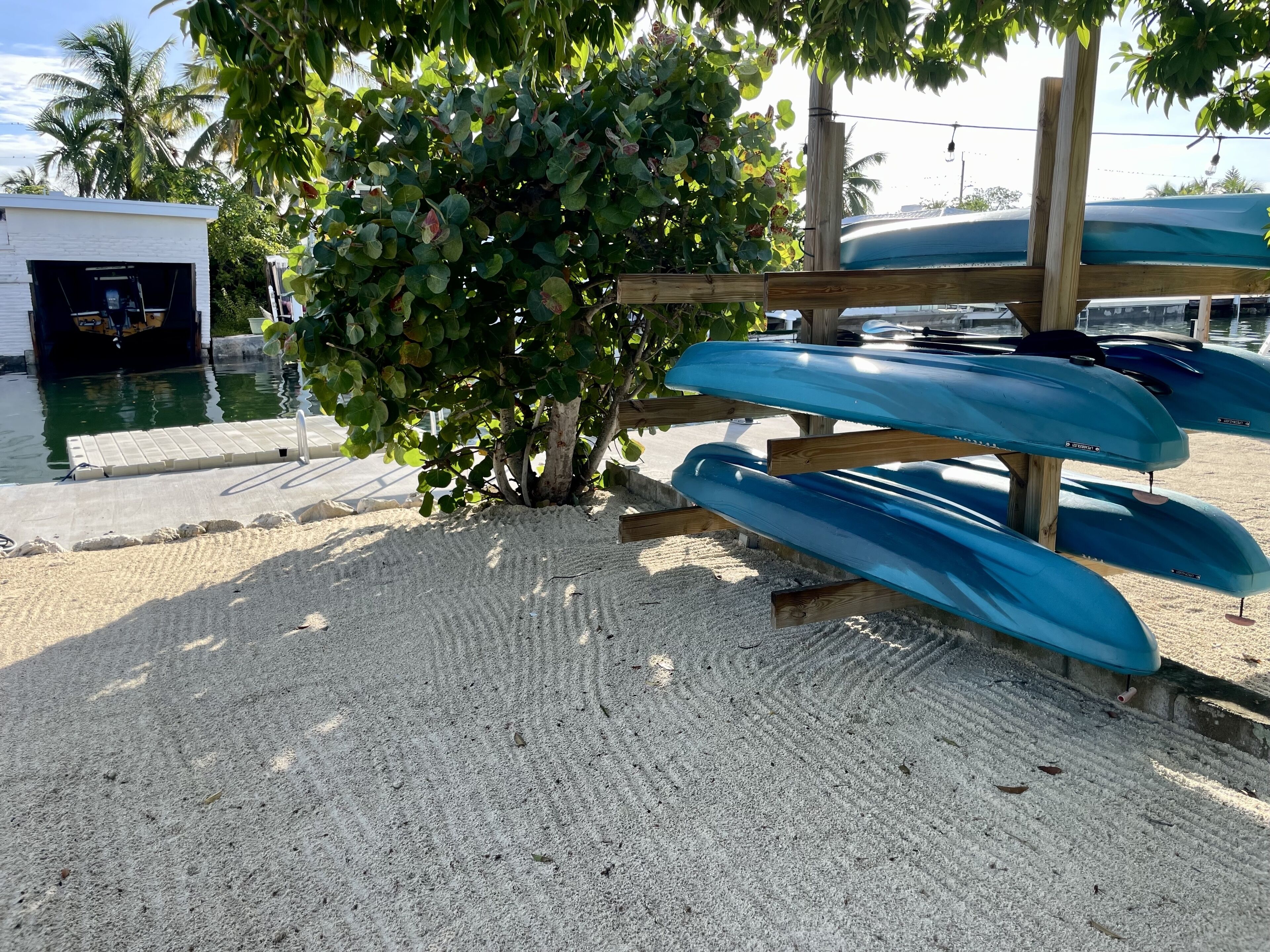 A sandy beach area with a wooden structure holding several blue kayaks.