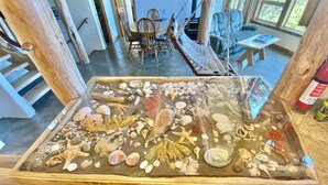 A room with a glass display table filled with seashells and corals, a wooden dining table with chairs, a sofa, and a fireplace. - Stunning Custom Cabin in the woods; Mountain and Ocean Views! (Brookings)