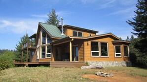 A modern wooden house with a green roof, large windows, and a deck. - Stunning Custom Cabin in the woods; Mountain and Ocean Views! (Brookings)