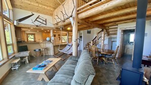 A spacious living area with a large gray sofa, a dining table with chairs, a hanging hammock, and a fireplace. - Stunning Custom Cabin in the woods; Mountain and Ocean Views! (Brookings)