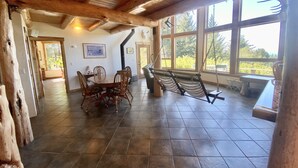 A spacious dining area with a wooden table and chairs, a hammock, and large windows offering a view of the outdoors. - Stunning Custom Cabin in the woods; Mountain and Ocean Views! (Brookings)