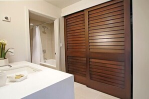 A bathroom with a white sink, a shower, and a wooden door. - Location Location Location!Ekahi 32C!Designer Remodel 2bd 2 bth. Ocean View! (Wailea-Makena)