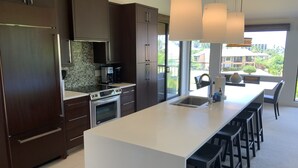 A modern kitchen with dark wood cabinets, a white countertop, stainless steel appliances, and a large island with bar stools. - Location Location Location!Ekahi 32C!Designer Remodel 2bd Remaining Fall $400/nt (Wailea-Makena)