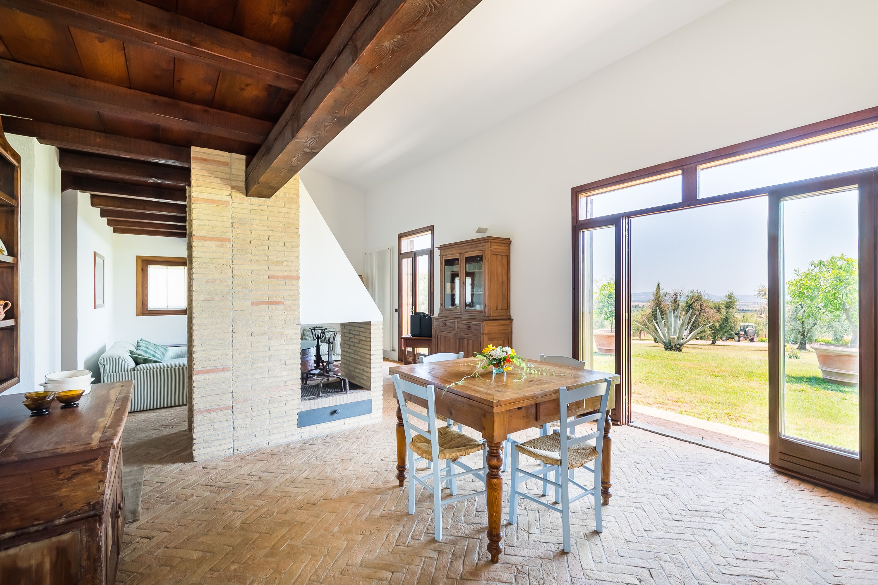 Un comedor amplio con una mesa y sillas de madera, una pared de ladrillo y un amplio ventanal corredero que da a un jardín.