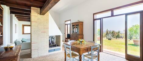 Un comedor amplio con una mesa y sillas de madera, una pared de ladrillo y un amplio ventanal corredero que da a un jardín.