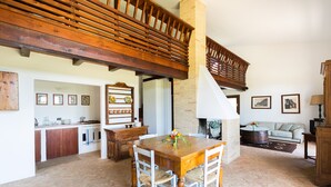 A spacious living area with a wooden dining table, white chairs, a fireplace, and a kitchen area with wooden cabinets and a herringbone floor pattern. - Villa with pool in the middle of Maremma (Magliano)