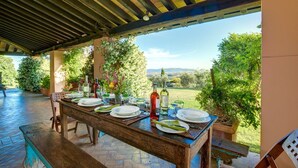 An outdoor dining area with a table set for four, surrounded by potted plants and a view of the countryside. - Villa with pool in the middle of Maremma (Magliano)