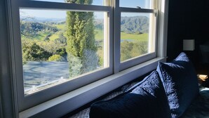 A room with a large window overlooking a scenic landscape, a bed with a blue quilt, and a lamp on the nightstand. - Stunning views in premier winery area. Very private with deck! (Paso Robles)