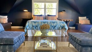 A bedroom with a sloped ceiling, a large bed with patterned bedding, two sofas, a small table with a vase, and two bedside lamps. - Stunning views in premier winery area. Very private with deck! (Paso Robles)