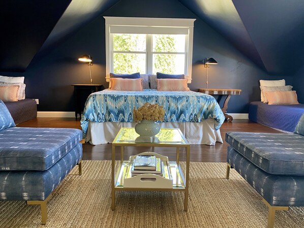 A bedroom with a sloped ceiling, a large bed with patterned bedding, two sofas, a small table with a vase, and two bedside lamps.