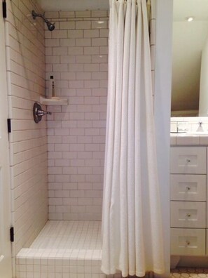 A bathroom with white subway tiles, a shower with a white curtain, and a vanity with drawers.
