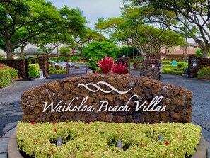 A sign for Waikoloa Beach Villas with a stone wall and greenery. - Luxury accommodations, discounted golf and beautiful sunsets year round. (Waikoloa Village)