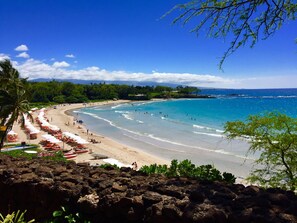 A beach with clear blue water, a sandy shore, and a line of umbrellas. - Luxury accommodations, discounted golf and beautiful sunsets year round. (Waikoloa Village)