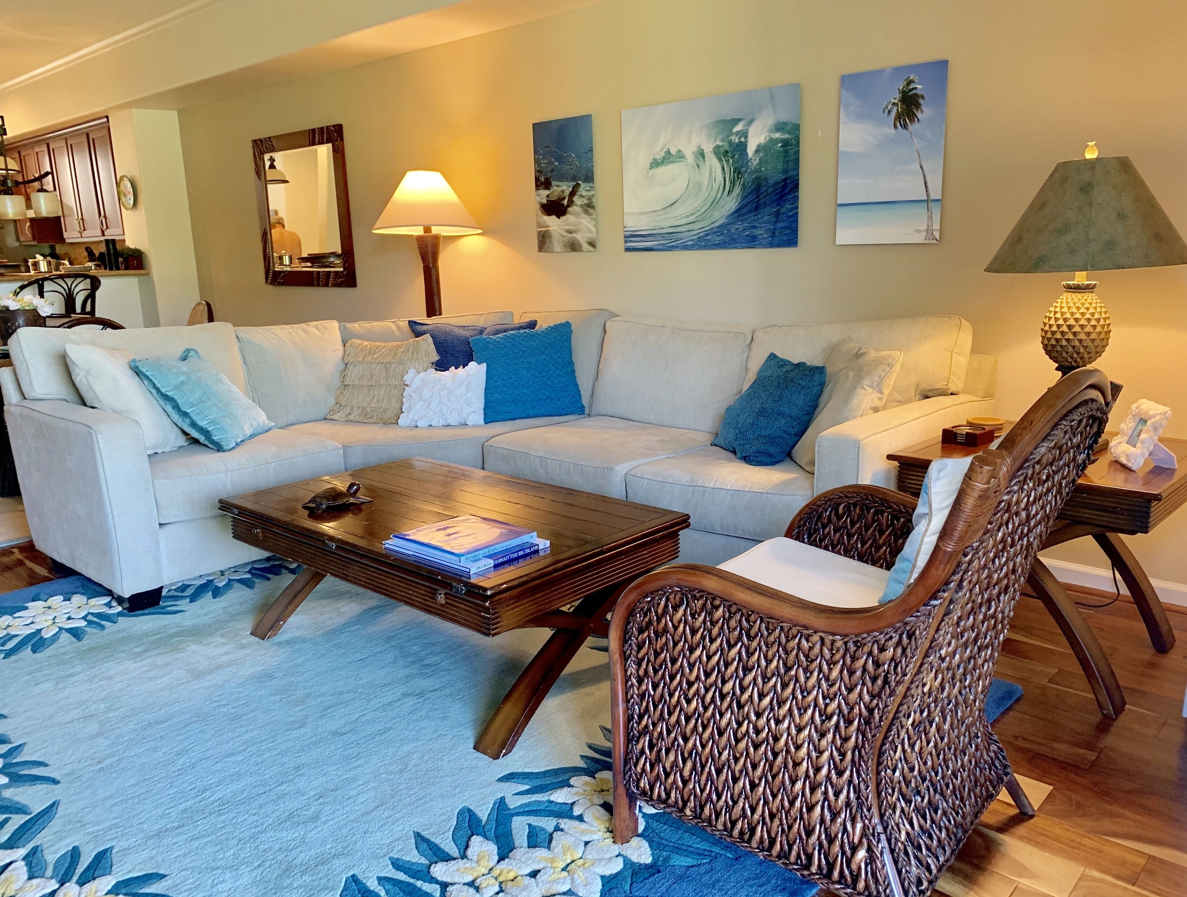 A living room with a sofa, coffee table, and wicker chair. There are wall art pieces and a lamp.