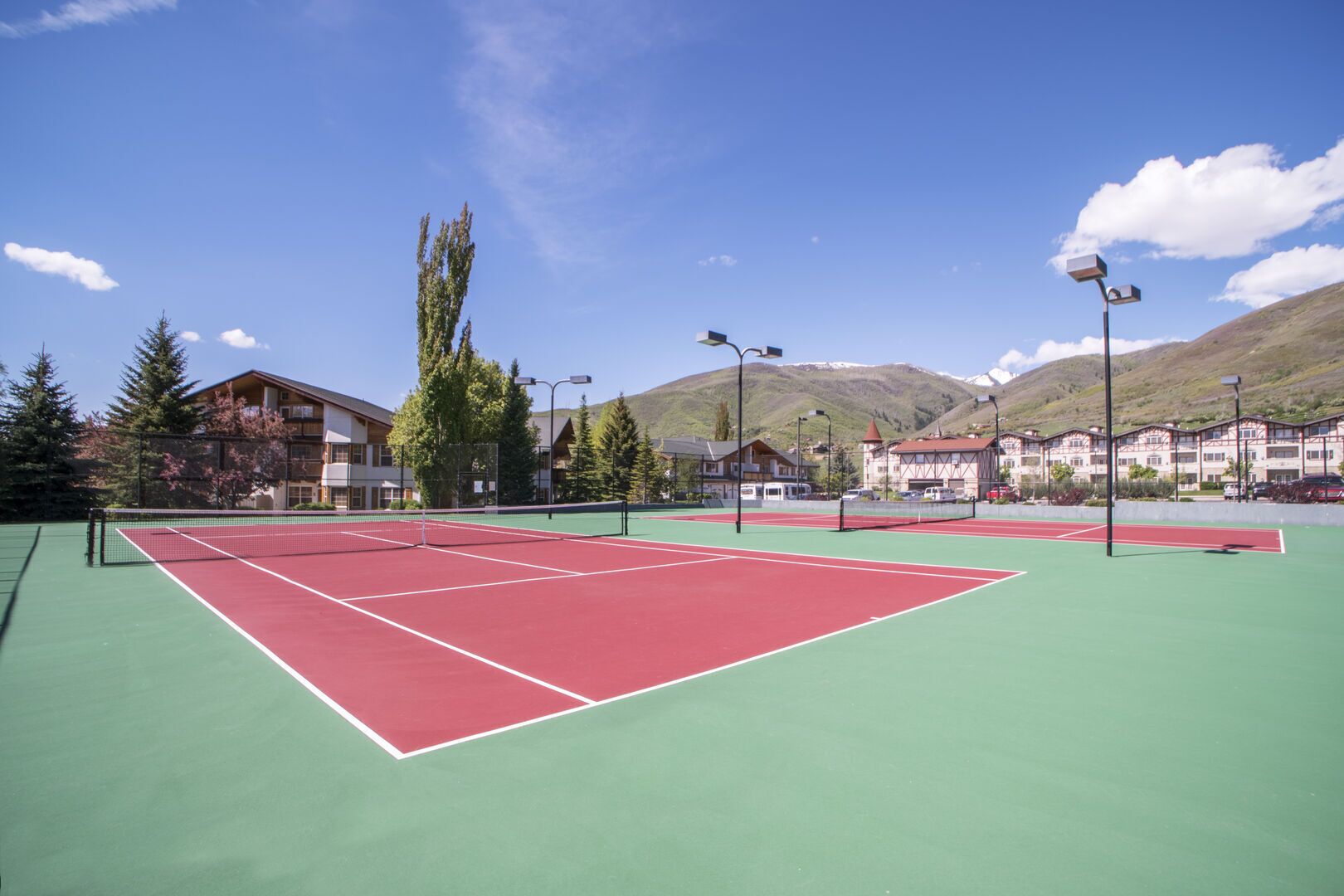 A tennis court with a net, surrounded by buildings and trees.