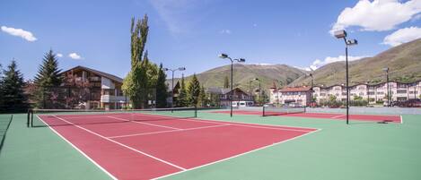 A tennis court with a net, surrounded by buildings and trees.