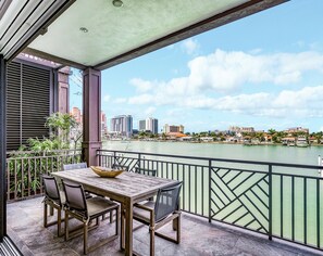 Ein Balkon mit Tisch und Stühlen, mit Blick auf einen Fluss und Gebäude im Hintergrund.