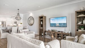 Ein geräumiger Wohnbereich mit großem Fernseher, bequemen Sitzmöglichkeiten, einer Holz-Unterhaltungseinheit und einer Küche im Hintergrund.