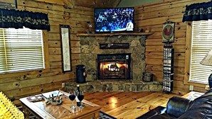 A cozy living room with a stone fireplace, wooden walls, a television, and a comfortable seating area. - Tree House Lodge-Real Log Mountain Paradise (Hiawassee)