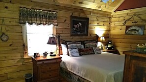 A cozy cabin-style bedroom with a wooden interior, a bed with multiple pillows, a nightstand with a lamp, and a window with a curtain. - Tree House Lodge-Real Log Mountain Paradise (Hiawassee)