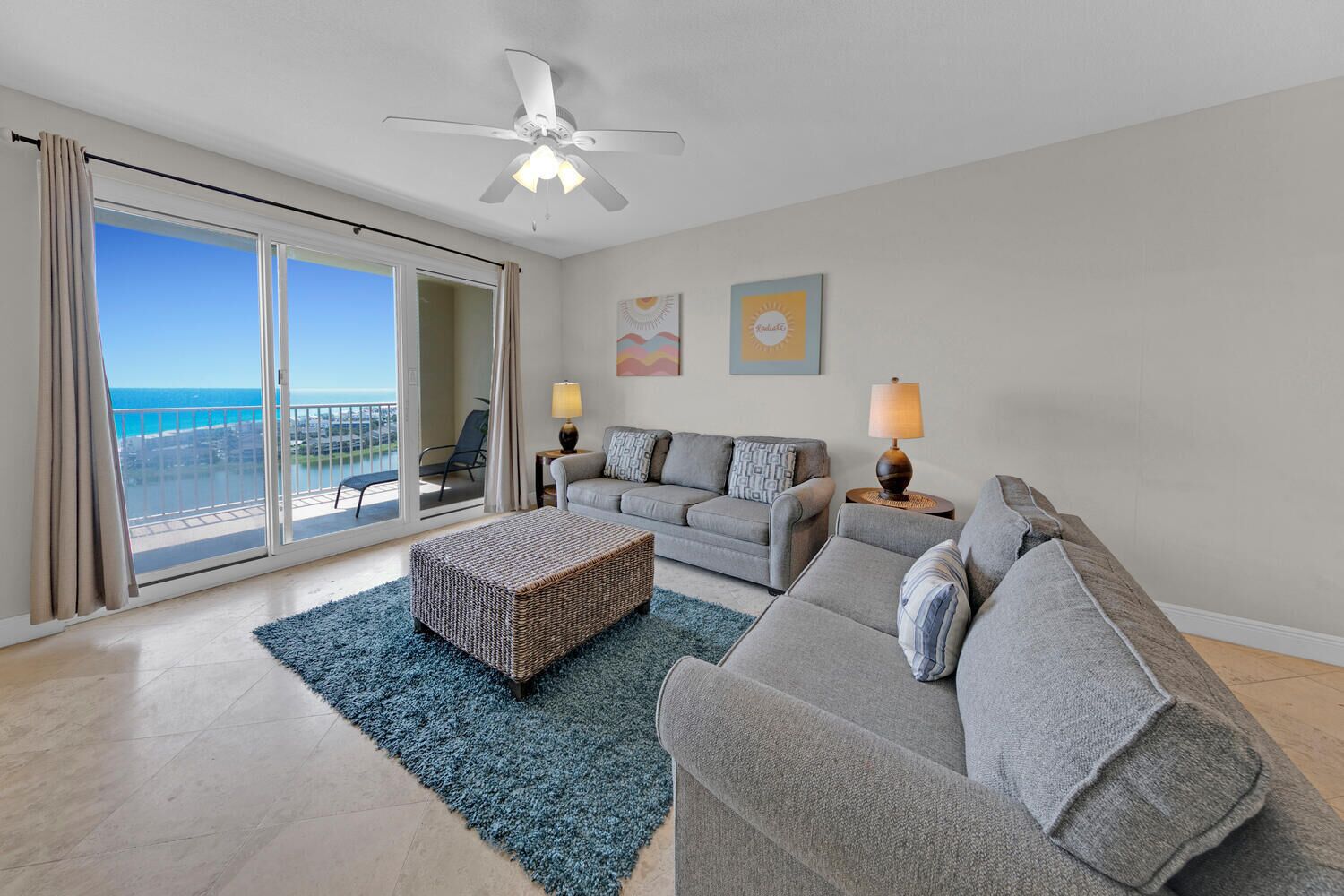 A living room with a balcony, a ceiling fan, and a view of the ocean.