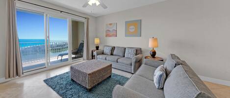 Un salon avec balcon, un ventilateur de plafond et vue sur l’océan.