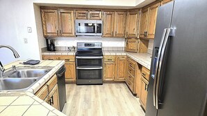 A kitchen with wooden cabinets, a stainless steel refrigerator, a microwave, an oven, and a sink.