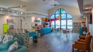 A spacious room with a large window, a blue sofa, a wooden floor, and a dining area with chairs and a table.