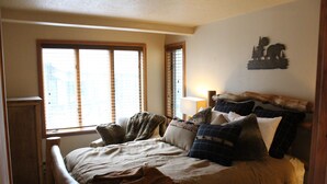 Un dormitorio con cama, mesita de noche, lámpara y ventana con persianas.